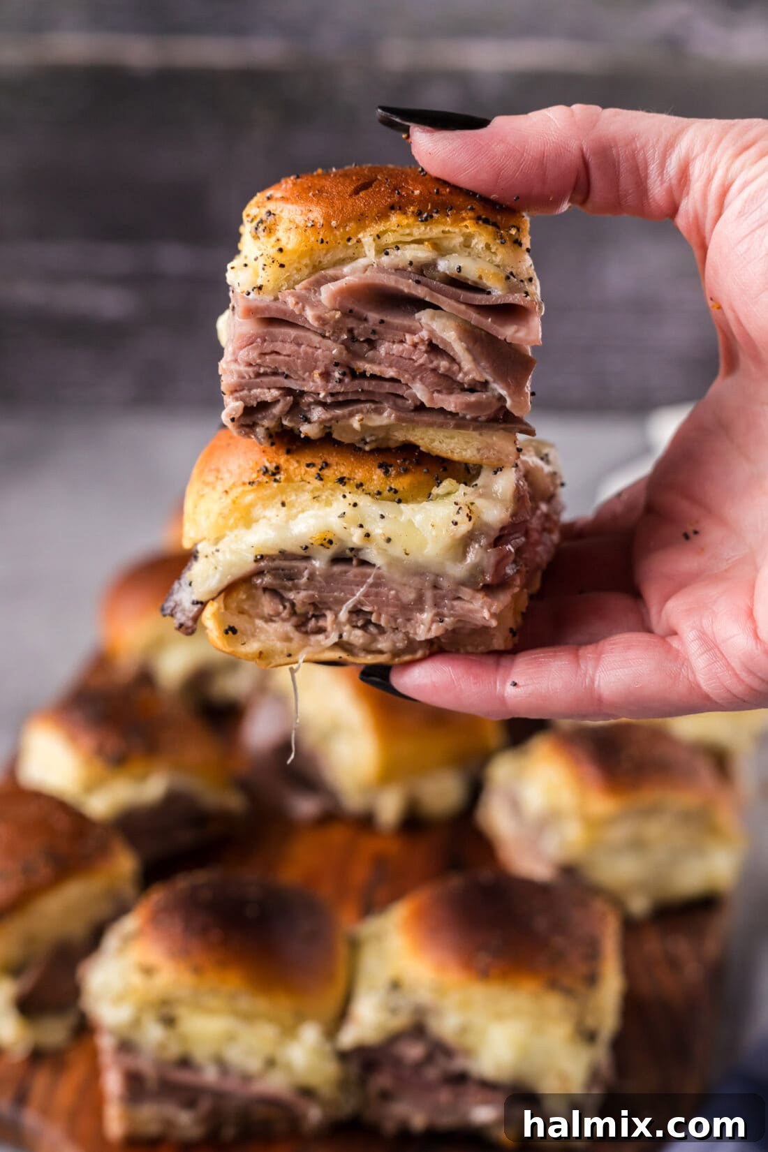 Hand holding up two perfectly baked Roast Beef Sliders, golden brown and ready to serve