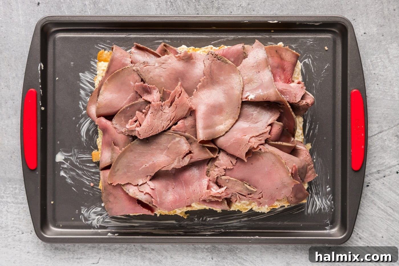 Sliced deli roast beef neatly arranged on top of slider buns, forming the savory layer