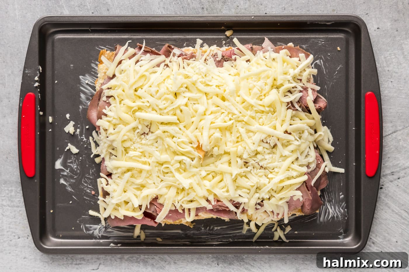 Shredded mozzarella cheese generously sprinkled over roast beef on slider buns, ready for melting