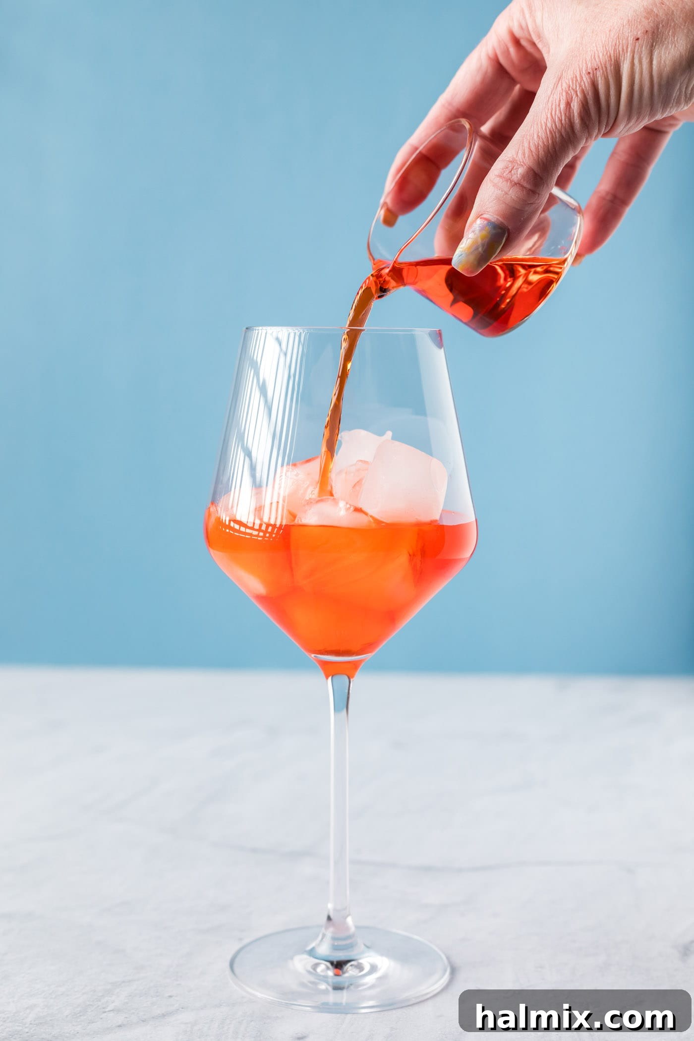 pouring Aperol into a wine glass with ice