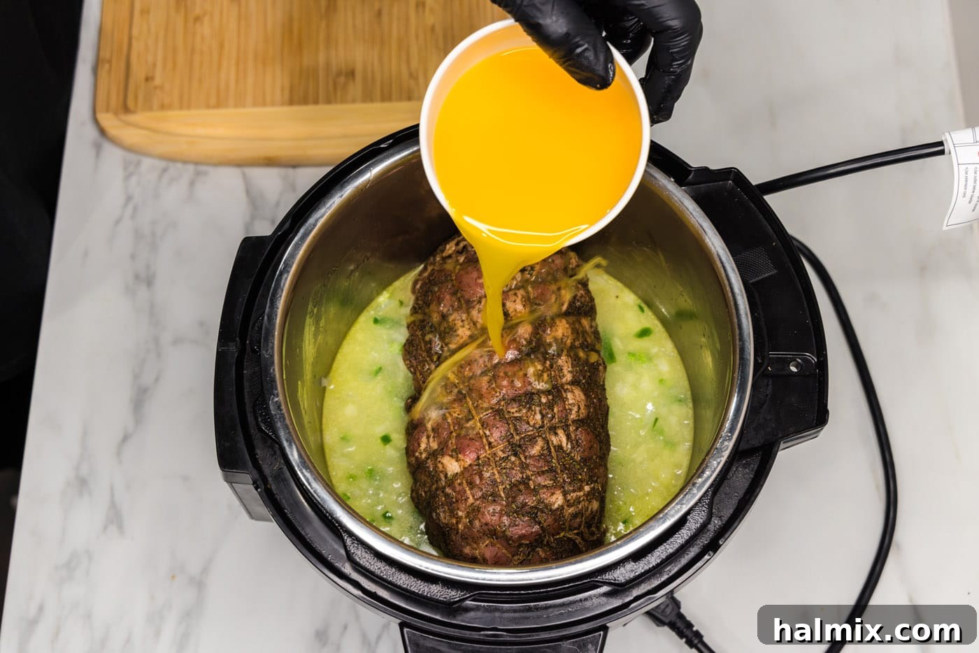 Crispy Instant Pot Carnitas 12 pouring orange juice into instant pot with jalapeno, onion, and pork roast