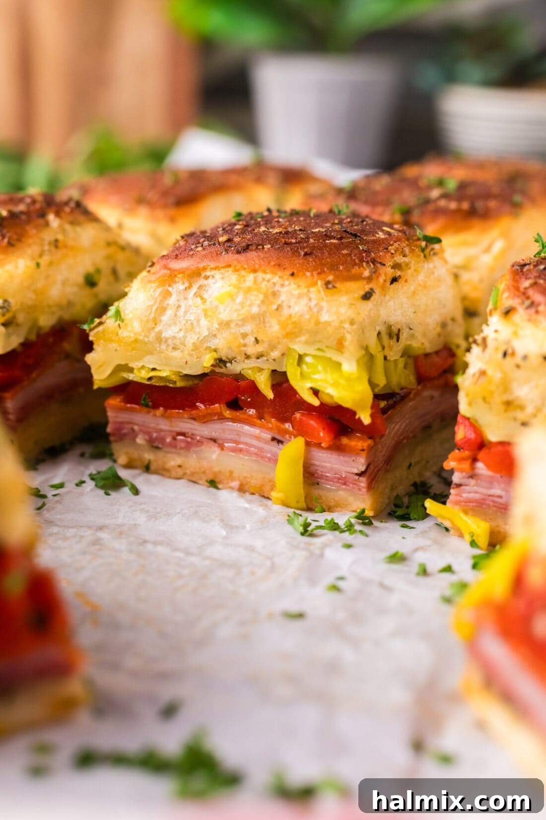 Close-up photo of baked Italian Sliders on parchment paper, showing melted cheese and toasted buns.
