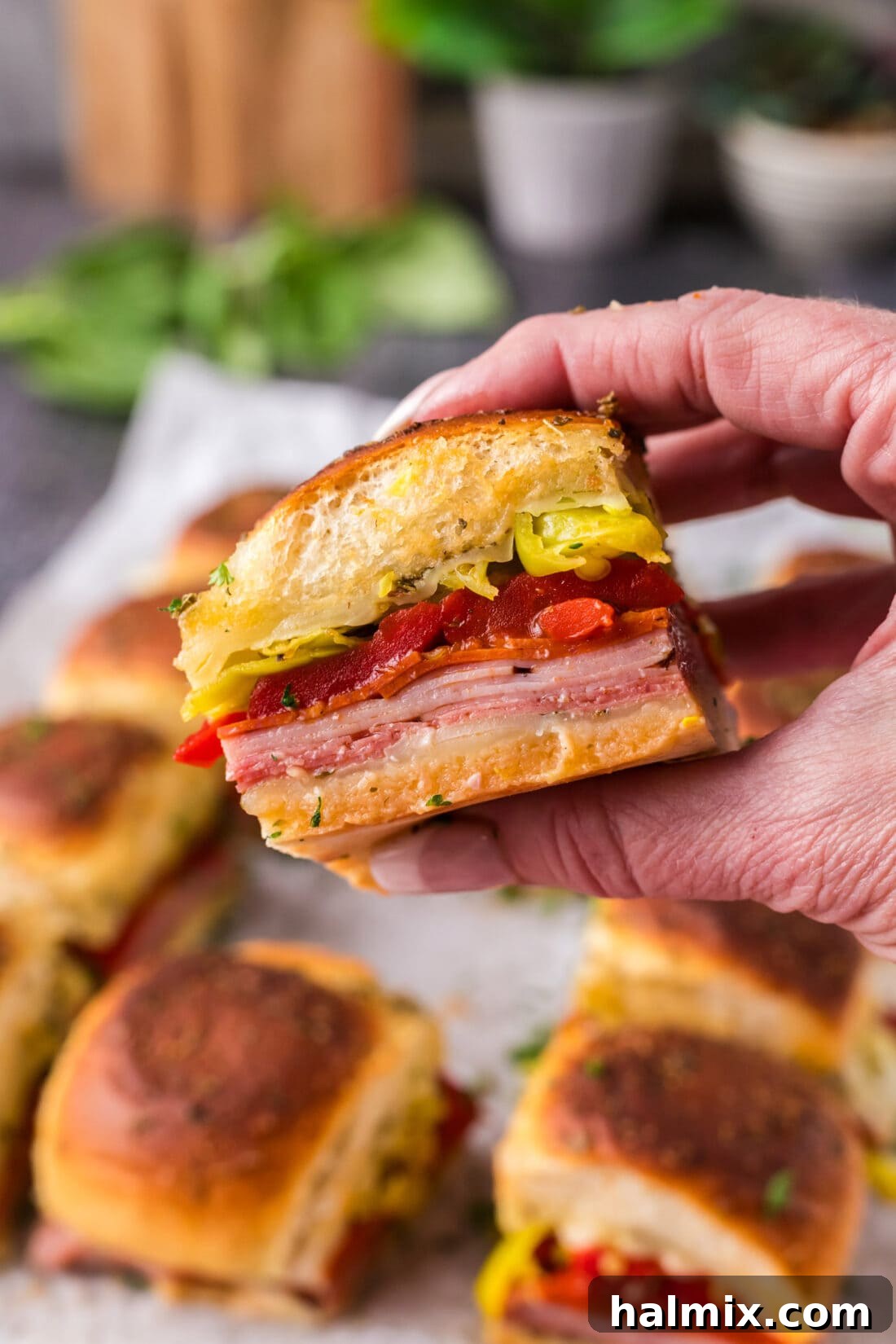 Hand holding up a single Italian Slider, showing off the layers of meat and cheese.