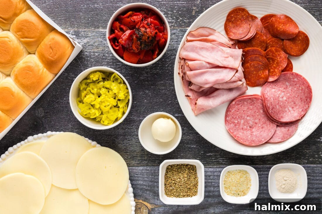 Spread of fresh ingredients for Italian Sliders on a cutting board, including buns, cheese, meats, and peppers.