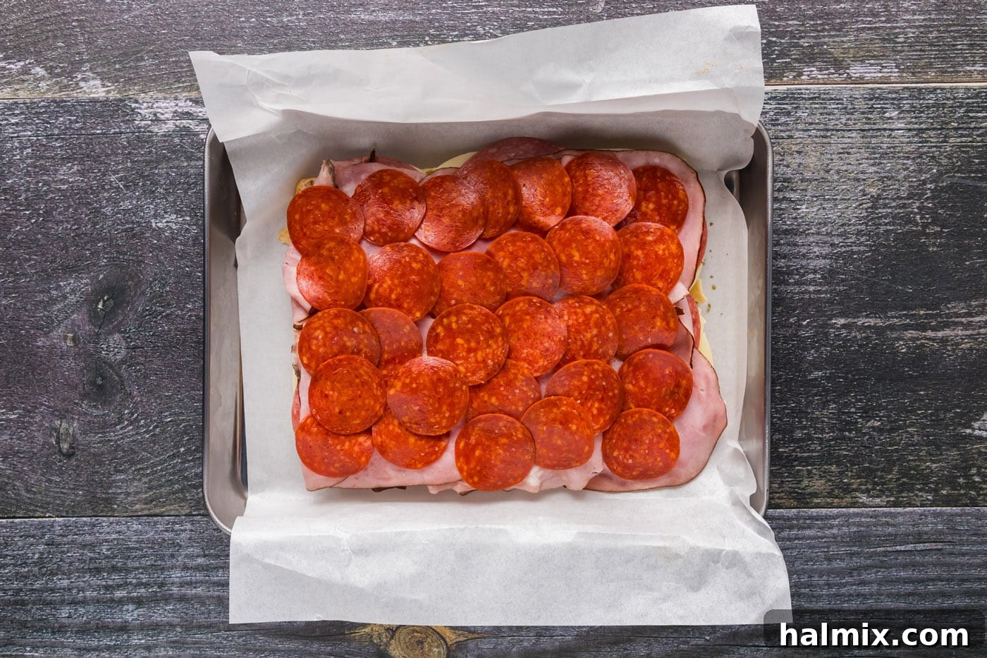 Pepperoni slices added over ham and salami layers on the sliders.