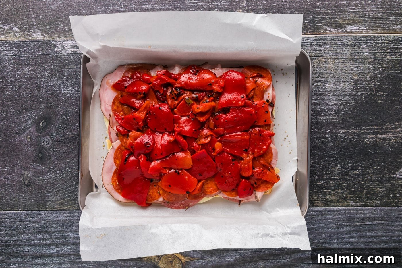 Roasted red bell peppers spread on top of the salami, ham, and pepperoni layers.