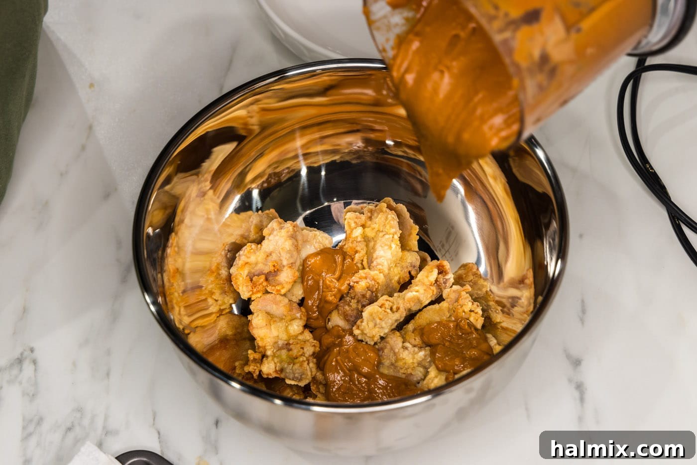 pouring peanut butter sauce over fried chicken