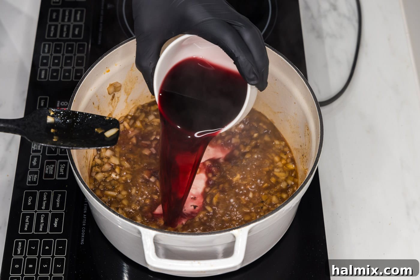 Red wine is being poured into the braising liquid mixture in a Dutch oven, adding depth to the sauce.
