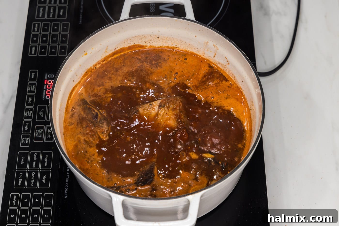 Braised Mexican beef short ribs are nestled in the rich liquid within a Dutch oven, ready for slow cooking.