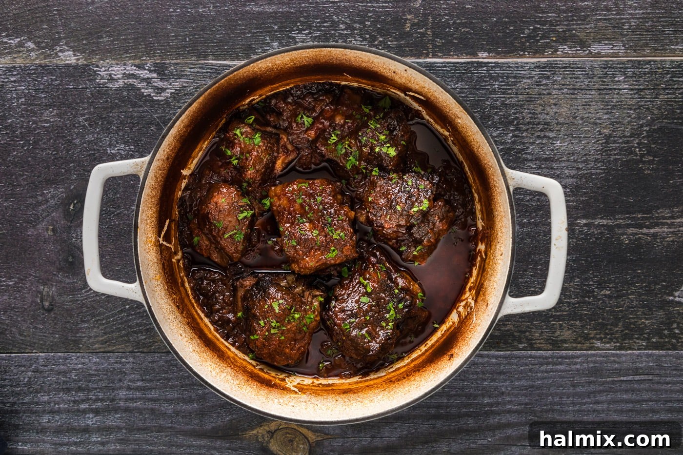 Finished Mexican short ribs are presented in a Dutch oven, ready to be served, with the rich sauce simmering around them.