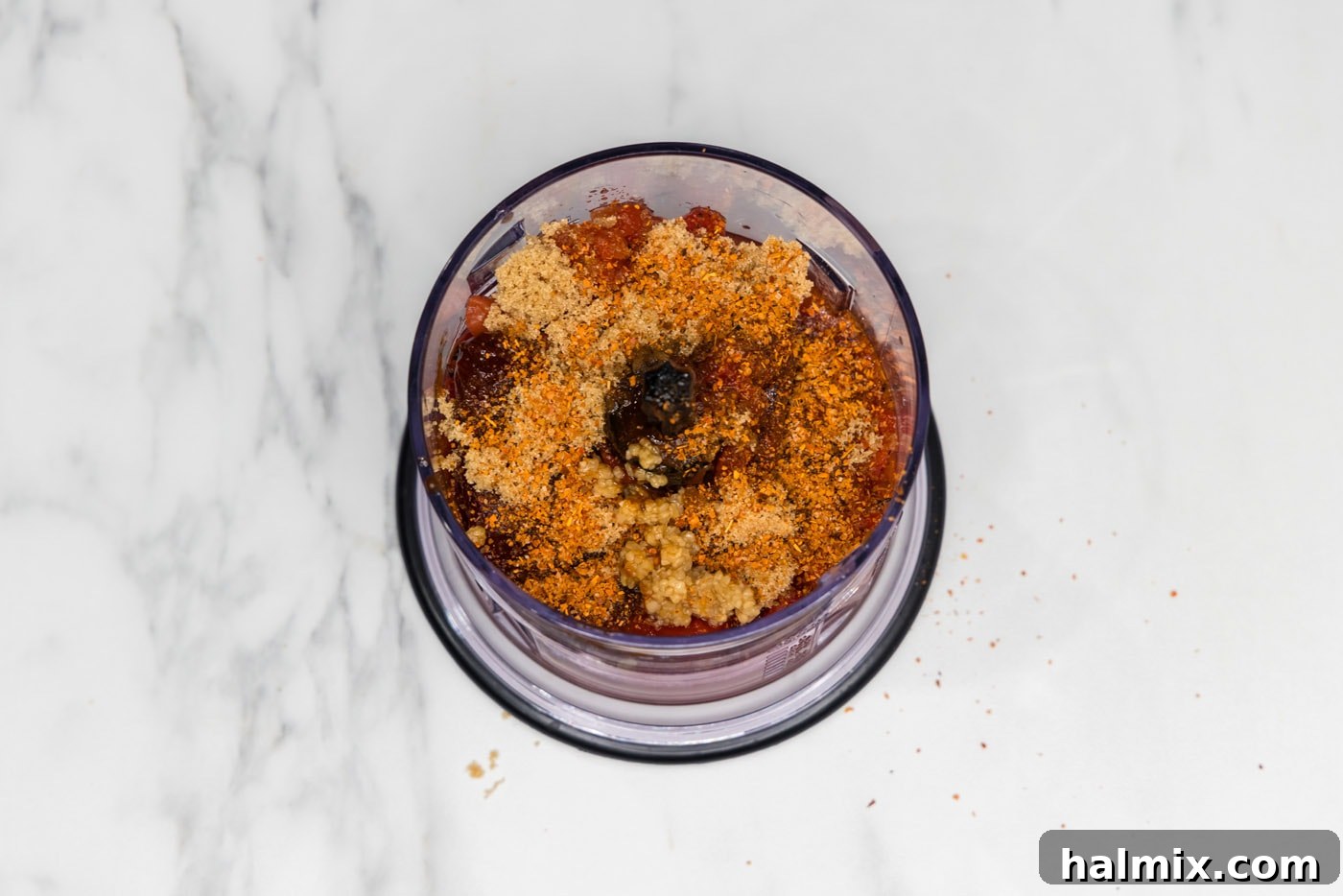 Canned tomatoes, chipotles, brown sugar, Cajun seasoning, and garlic are placed into a mini chopper, ready to be blended.