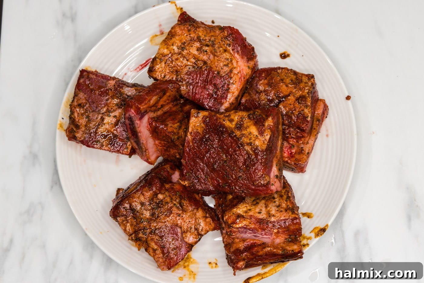 Seasoned short ribs are neatly arranged on a plate, ready for searing.