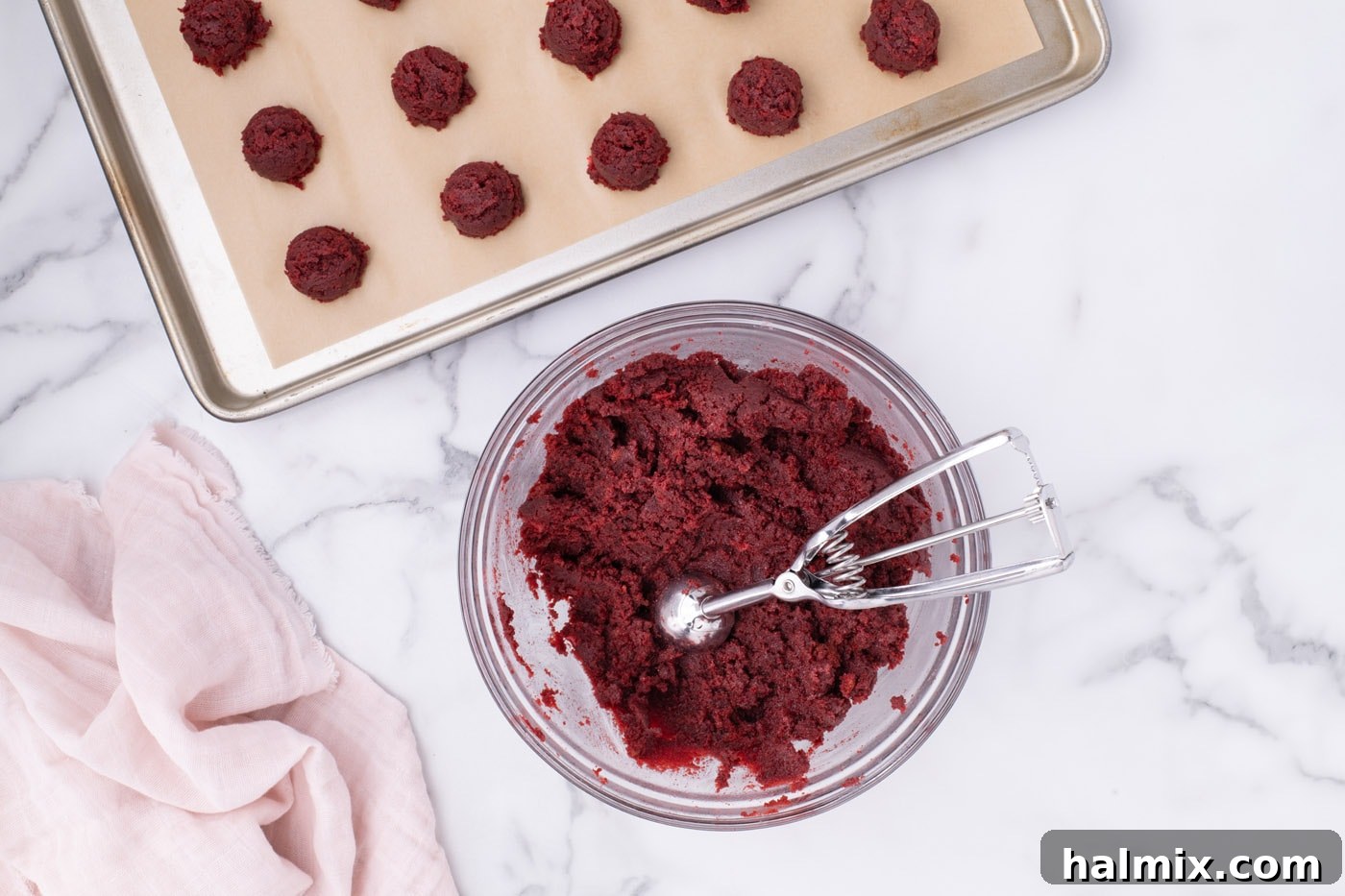 Using a cookie dough scoop to portion red velvet cake ball mixture onto a baking sheet