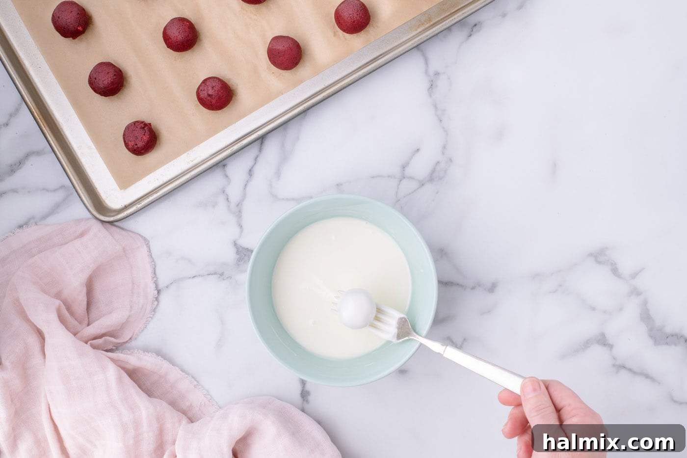 Dipping a red velvet cake ball into melted white chocolate using a fork
