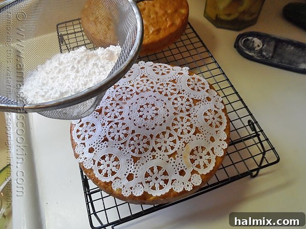 Powdered sugar being delicately sprinkled over a Merryfield apple cake using a paper doily for an elegant design.