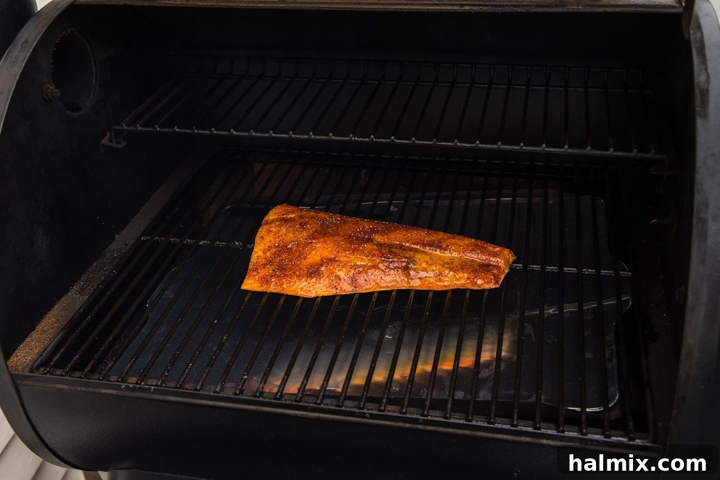 A seasoned salmon fillet placed skin-side down on smoker grates