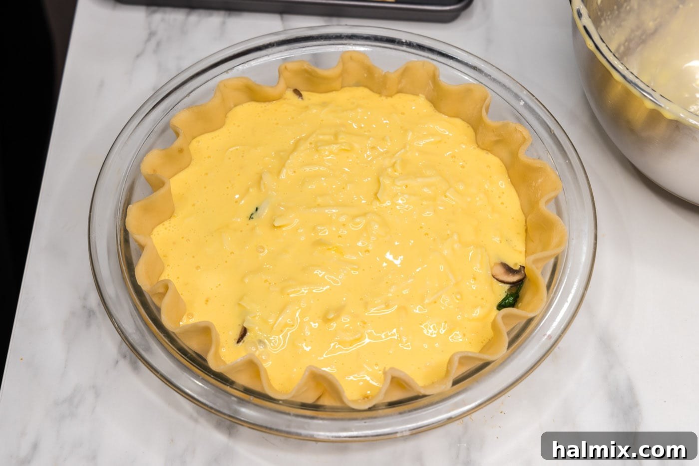 The rich egg and cheese filling being poured carefully over the first layer of spinach and mushrooms in the pie crust.