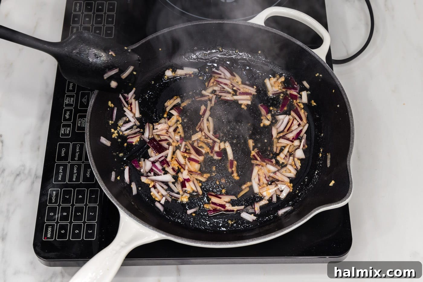 Close-up photo of red onion and minced garlic sautéing in melted butter in a skillet until tender and fragrant.