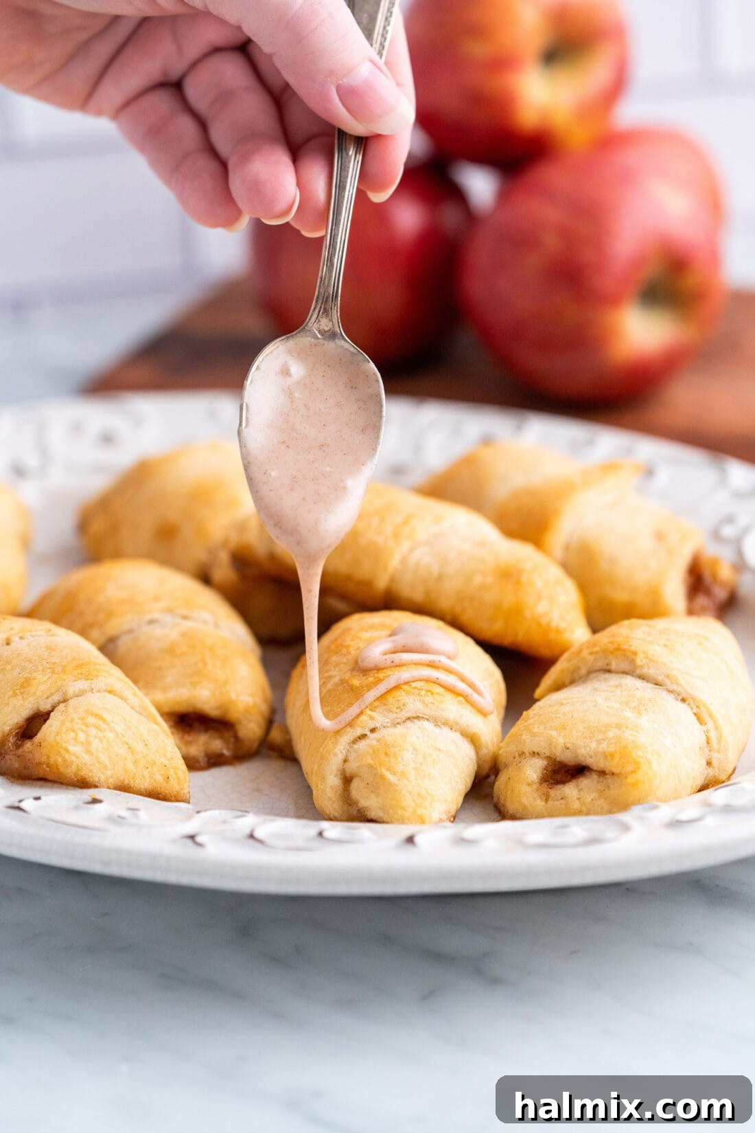 Drizzling sweet cinnamon glaze over a batch of warm apple pie bites on a wire rack.