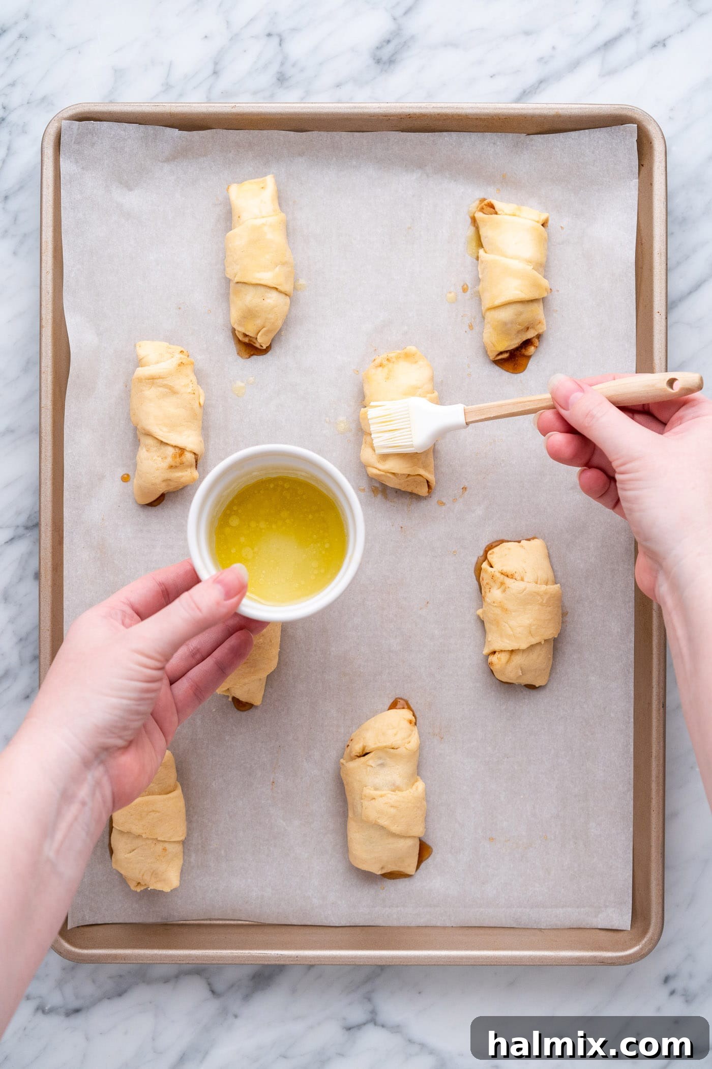 Brushing the tops of the rolled apple pie bites with melted butter before baking.