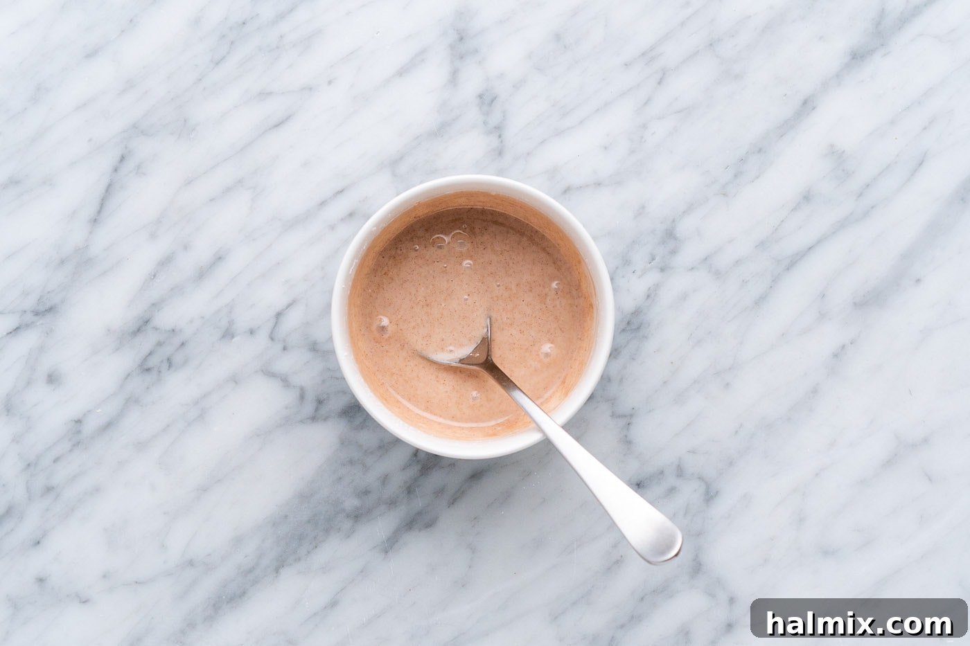 A bowl of smooth cinnamon glaze with a spoon, ready to be drizzled over the baked treats.