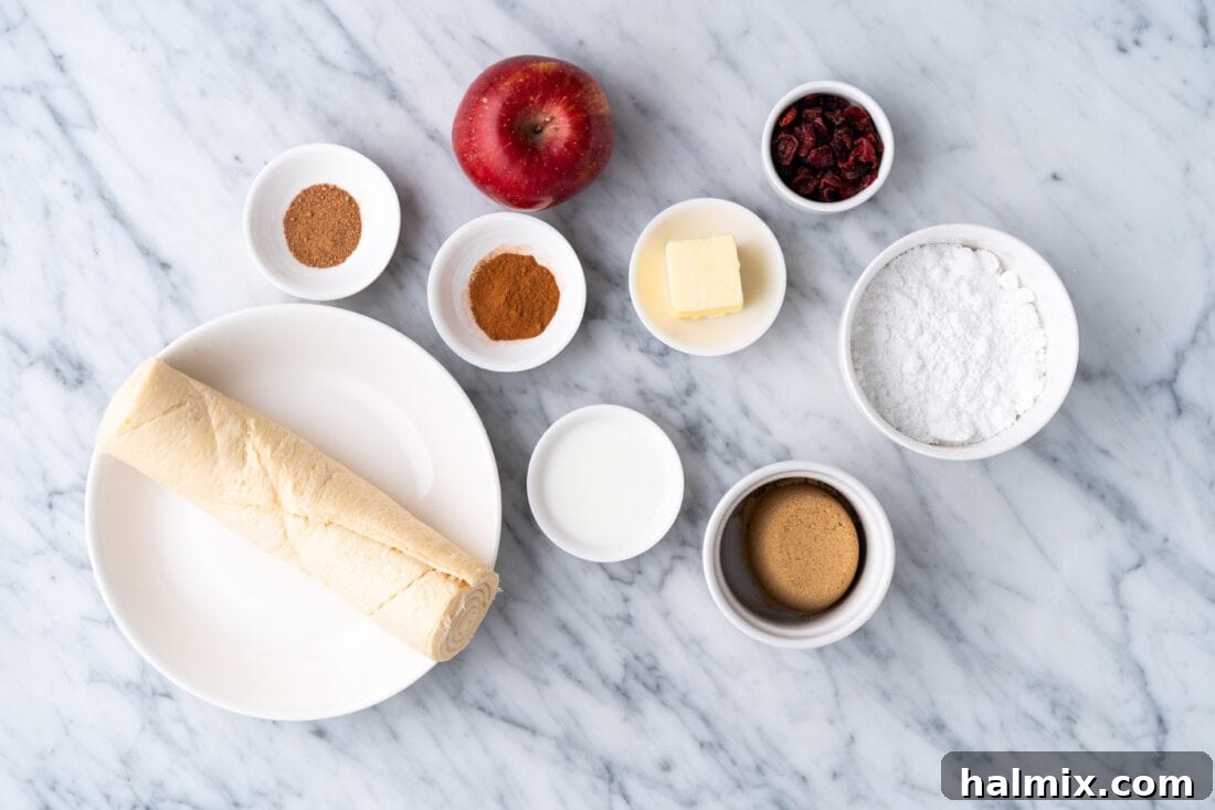 A flat lay photograph showcasing all the ingredients needed for apple pie bites: apples, butter, brown sugar, cinnamon, nutmeg, crescent rolls, powdered sugar, and milk.