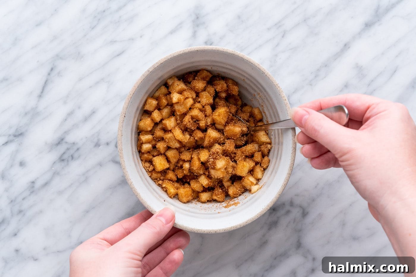 Diced apples mixed thoroughly with brown sugar and cinnamon in a bowl.