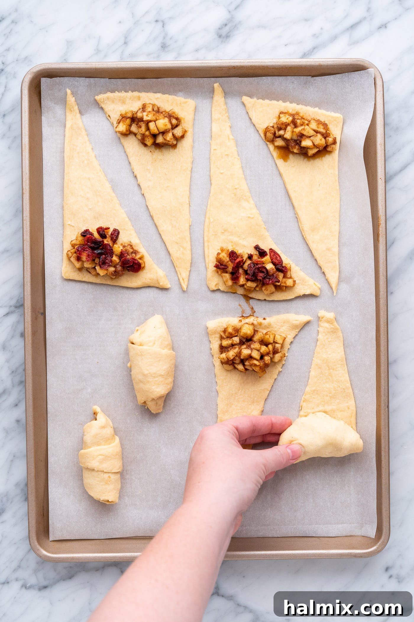 Rolling up the crescent roll triangles with the apple filling, sealing the edges for apple pie bites.