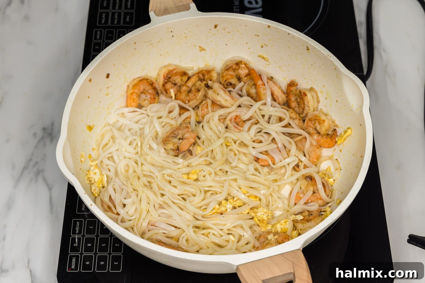 Cooked rice noodles being added to the skillet containing shrimp and scrambled egg.
