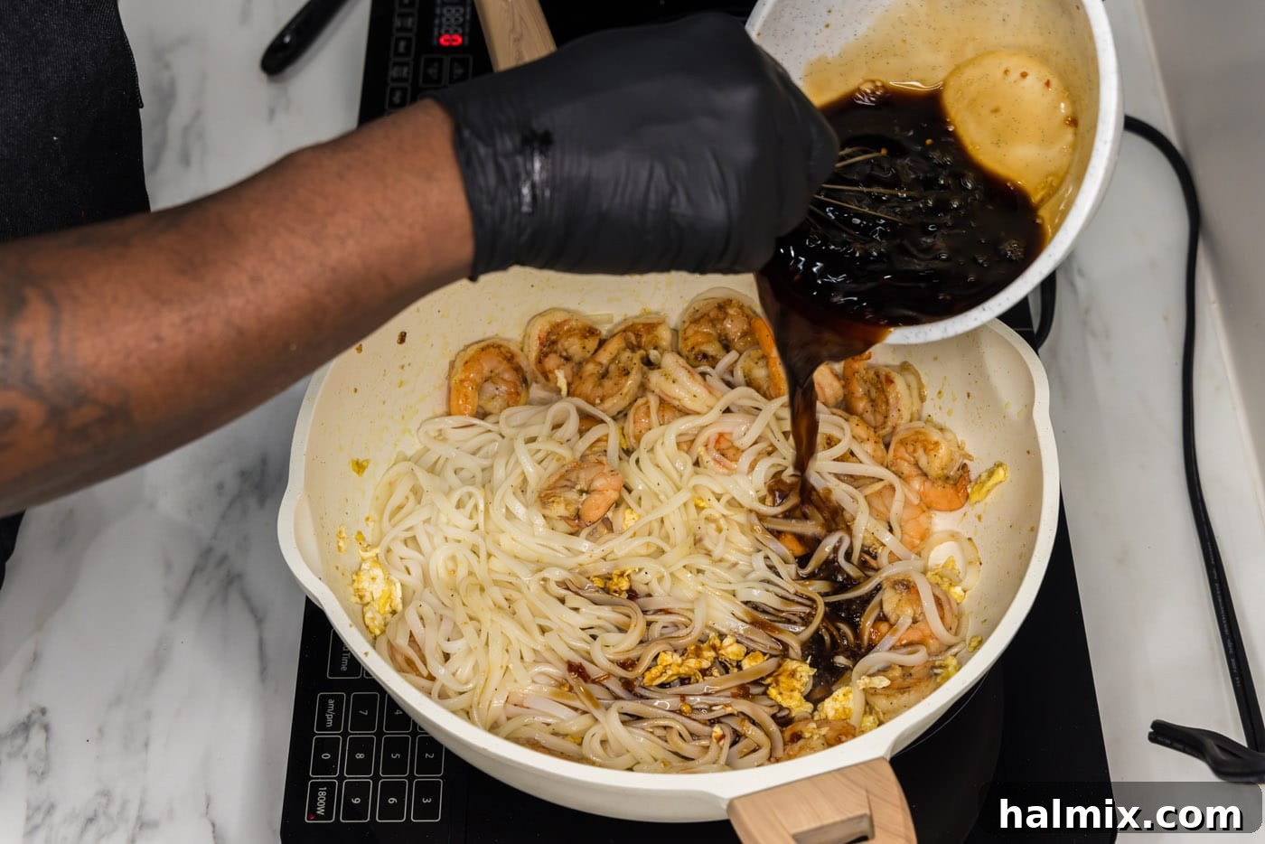 Vibrant Shrimp Pad Thai 10 The savory Pad Thai sauce being poured over the noodles, shrimp, and egg mixture in a large skillet.