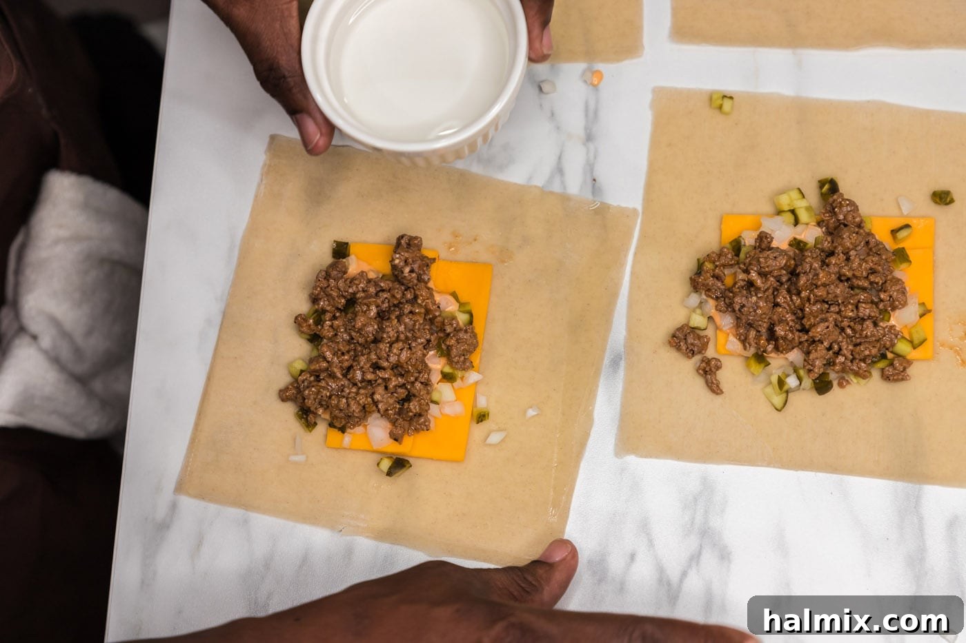 A finger applying water to the edges of an egg roll wrapper to moisten it for sealing.