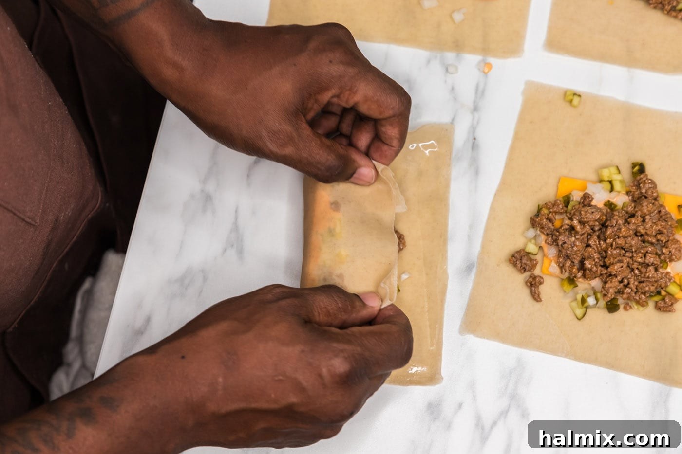 Hands demonstrating the initial fold of an egg roll wrapper over the filling.