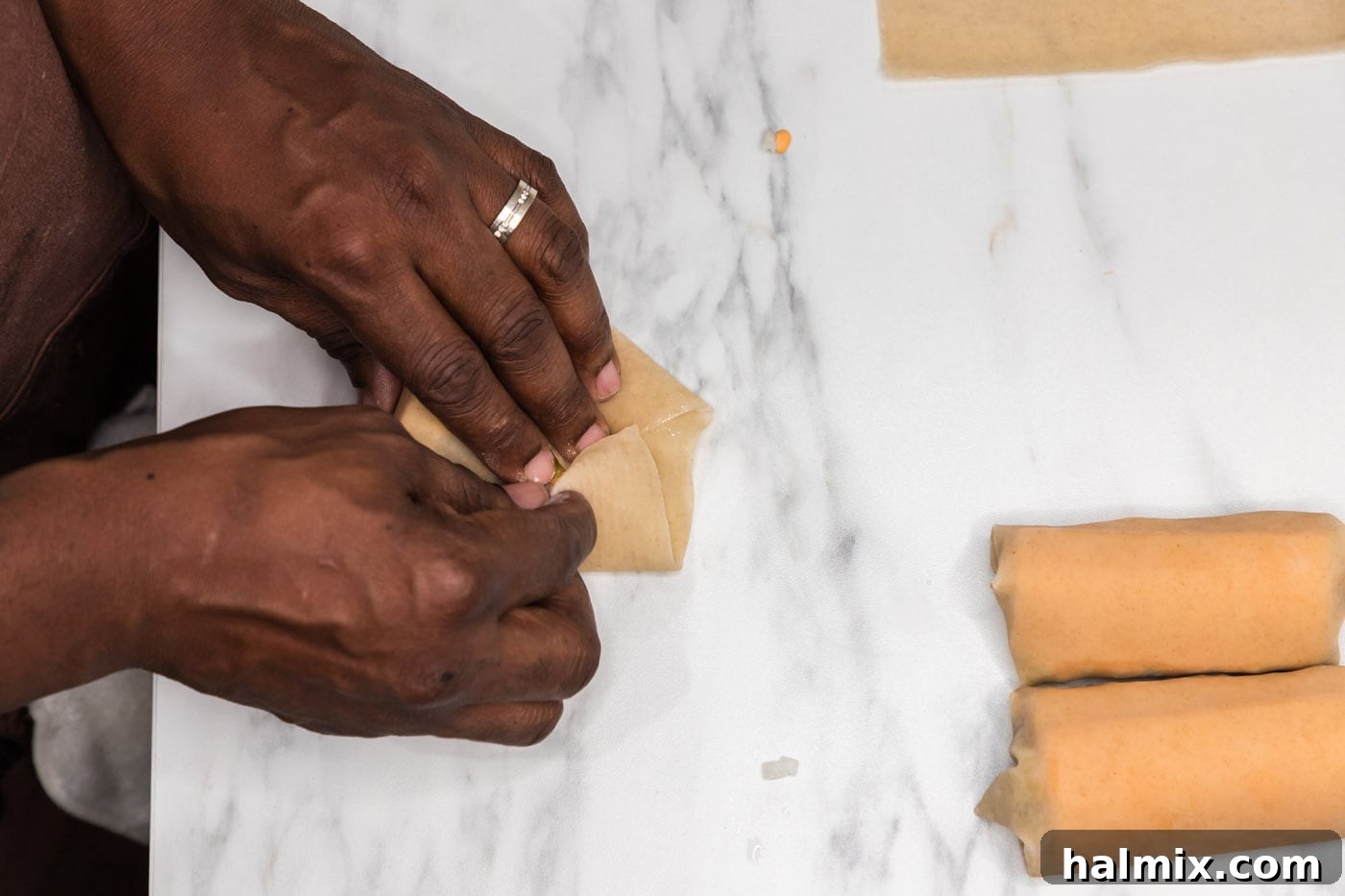 Hands completing the roll of an egg roll wrapper, sealing the ends to create a neat package.