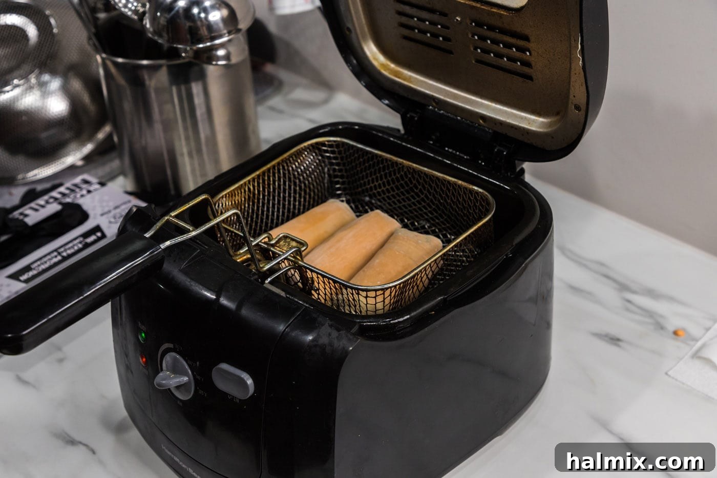 Several Big Mac Egg Rolls carefully lowered into hot oil in a deep fryer, beginning to cook and brown.