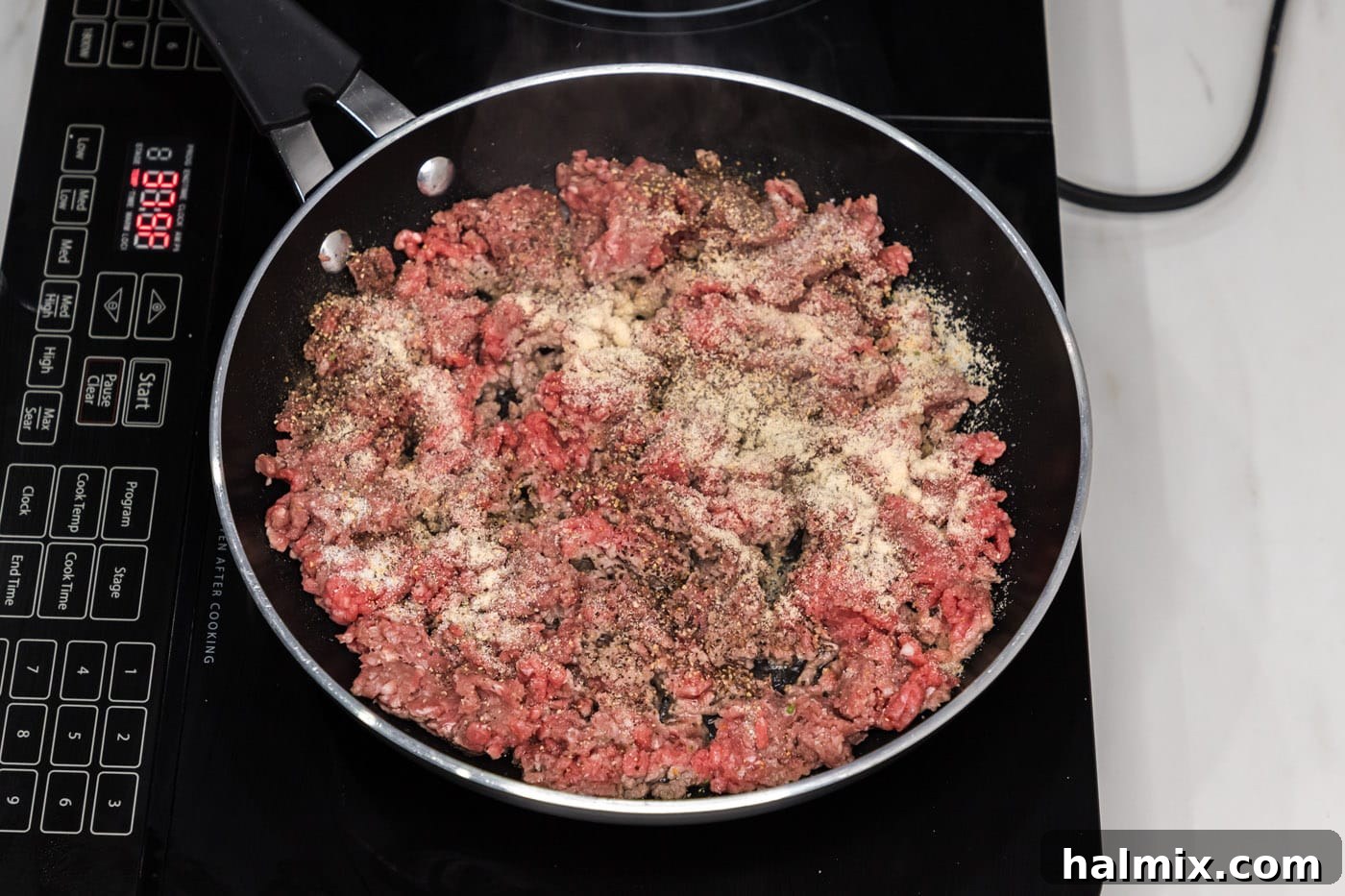 Ground beef cooking in a skillet with seasonings, beginning to brown.