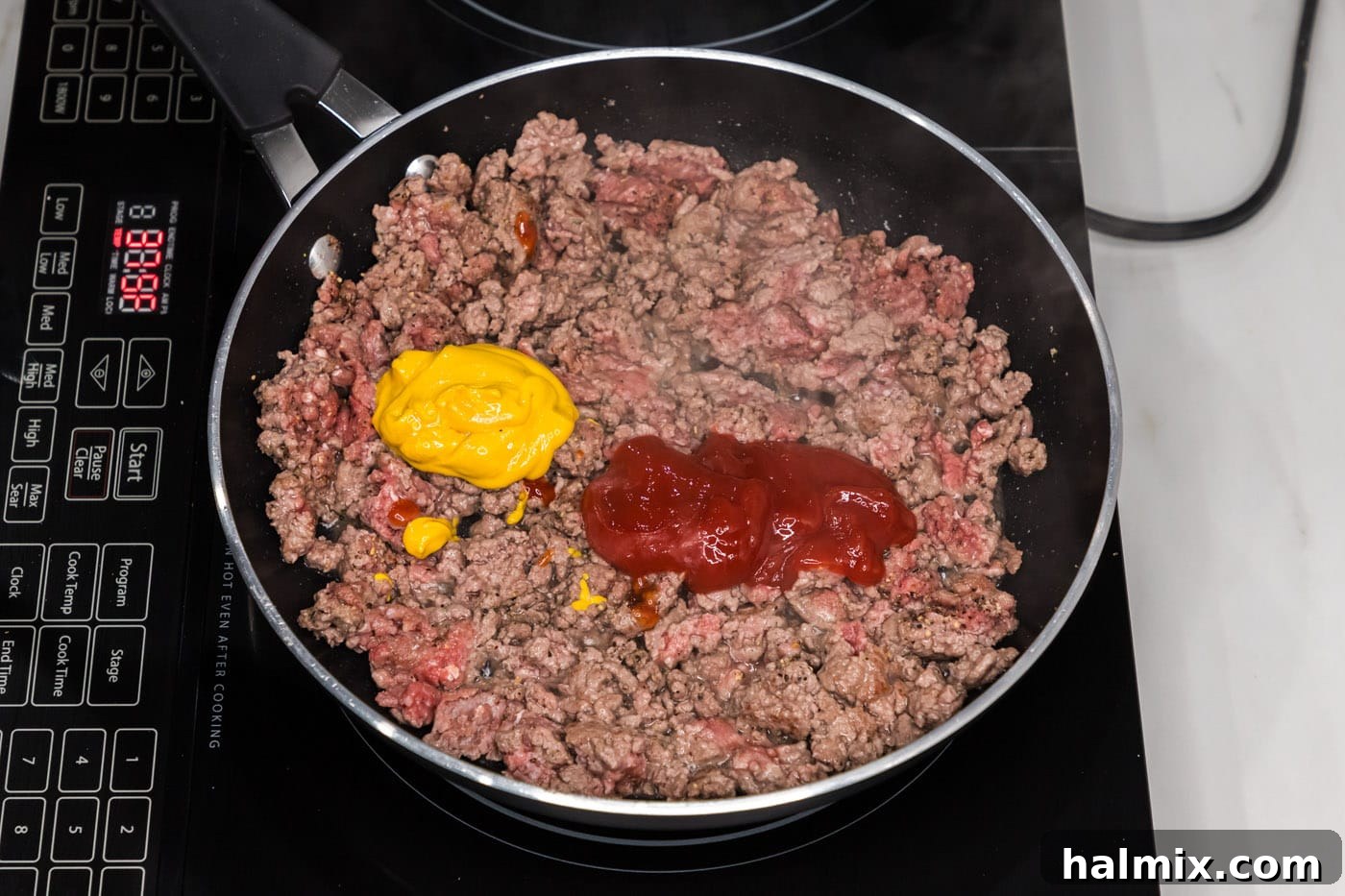 Ketchup and mustard being added to the browned ground beef in the skillet.