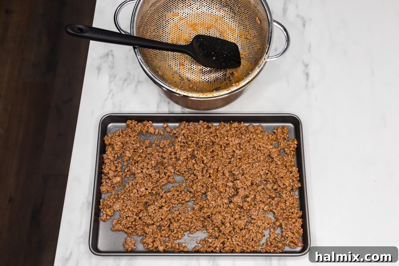 Transferring the drained ground beef mixture from the colander to a baking sheet to cool.