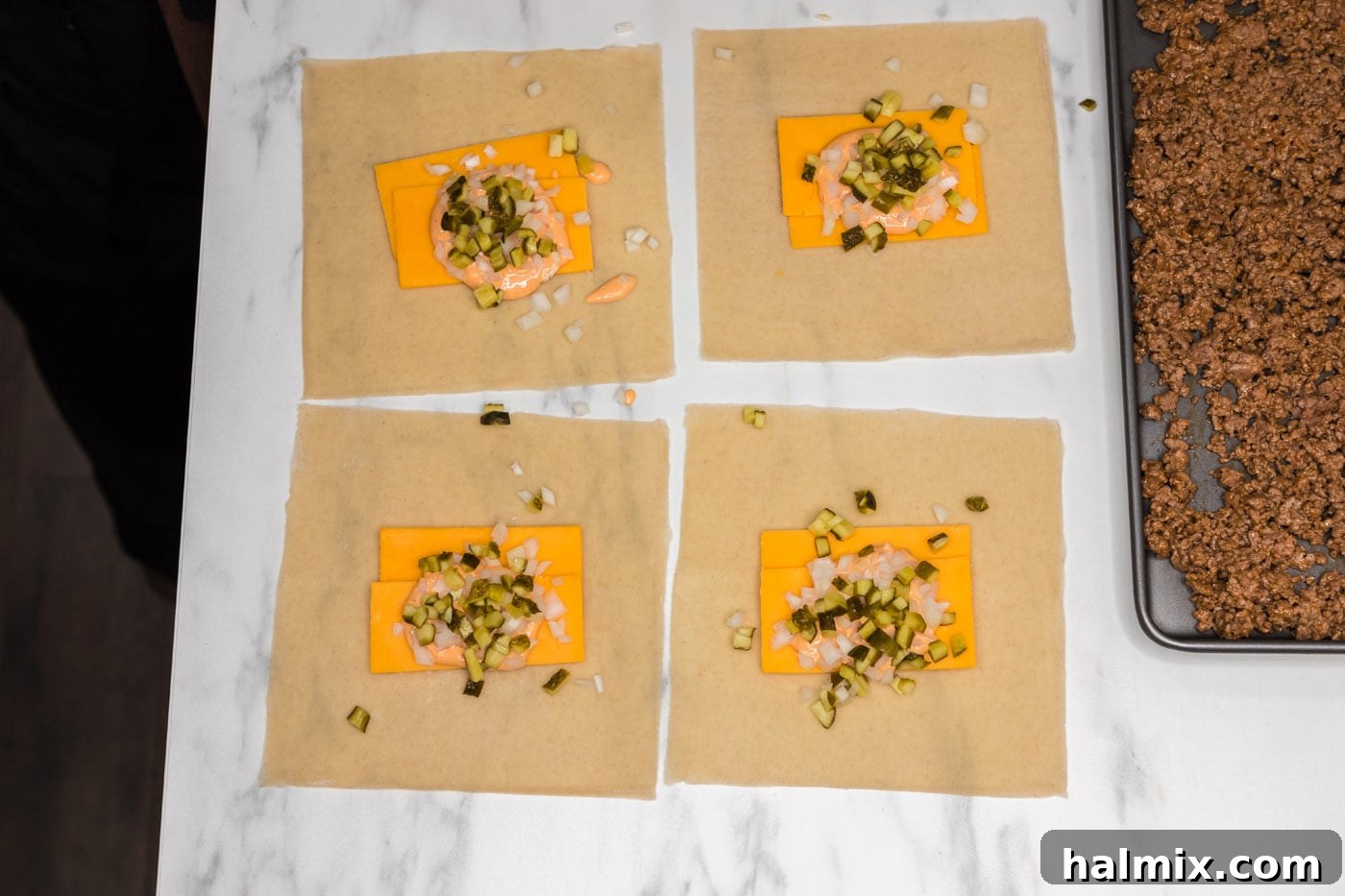 Egg roll wrappers laid out with cheddar cheese, chopped onion, and dill pickles placed in the center.