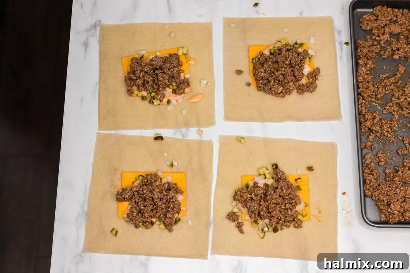Cooled ground beef added on top of the cheese, onion, and pickles on the egg roll wrappers.