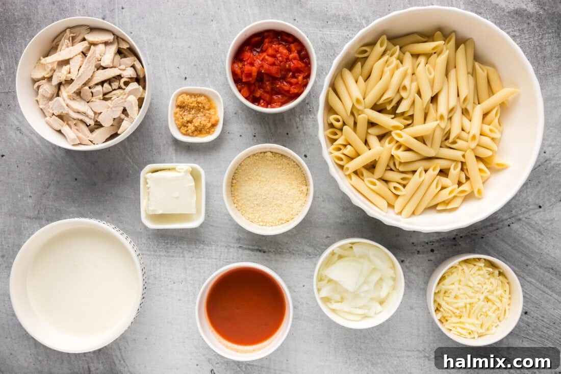 Various ingredients for Buffalo Chicken Pasta including pasta, chicken, cheeses, hot sauce, and aromatics laid out on a wooden surface.