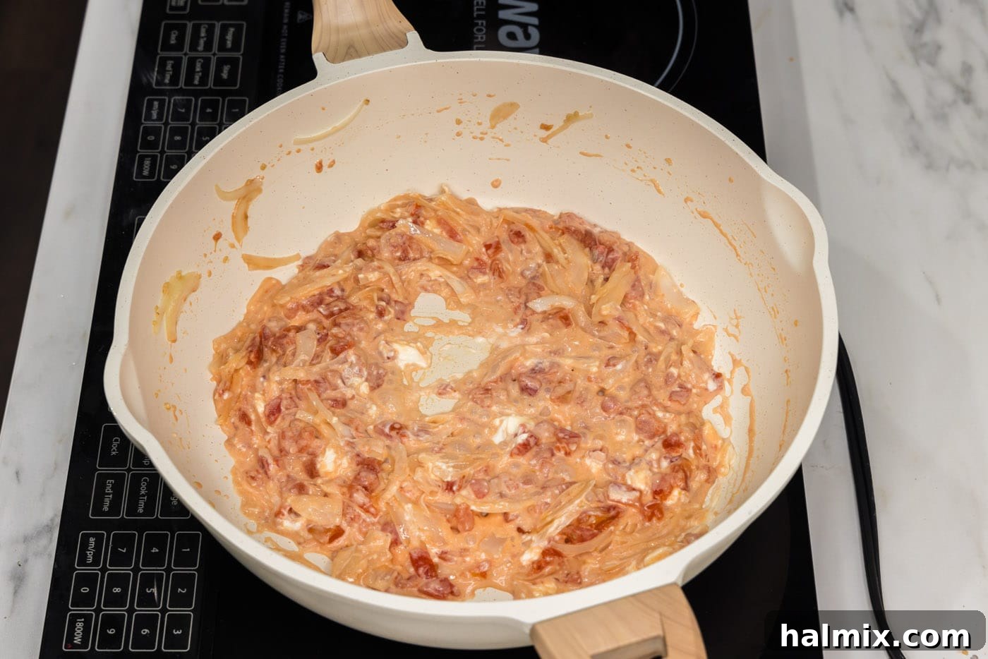 Cream cheese being stirred and smashed into the tomato, onion, and garlic mixture in a skillet, melting into the sauce.