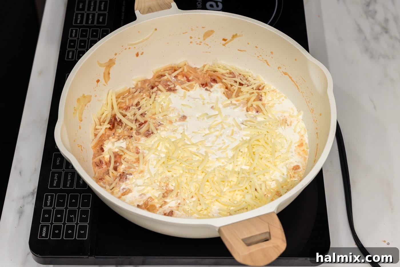 Heavy cream being poured into the skillet with the cream cheese, tomatoes, and aromatics, beginning to form the creamy sauce.