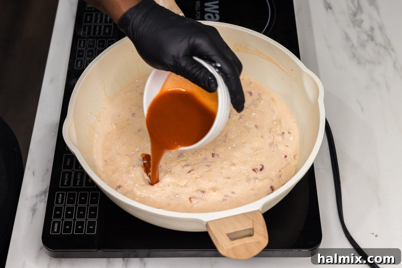 Hot sauce being added to the creamy mixture in the skillet, ready to be stirred into the buffalo sauce.