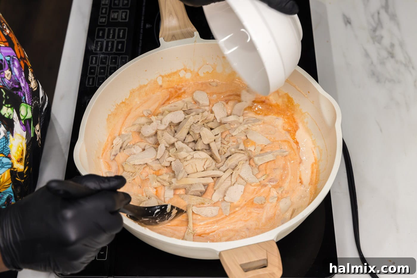 Chopped cooked chicken being stirred into the creamy buffalo sauce in a skillet, coating the chicken evenly.